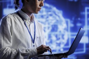 System administrator using laptop to maintenance artificial intelligence neural networks simulating human thought processes in computerized model. Adept professional doing checkup on AI systems
